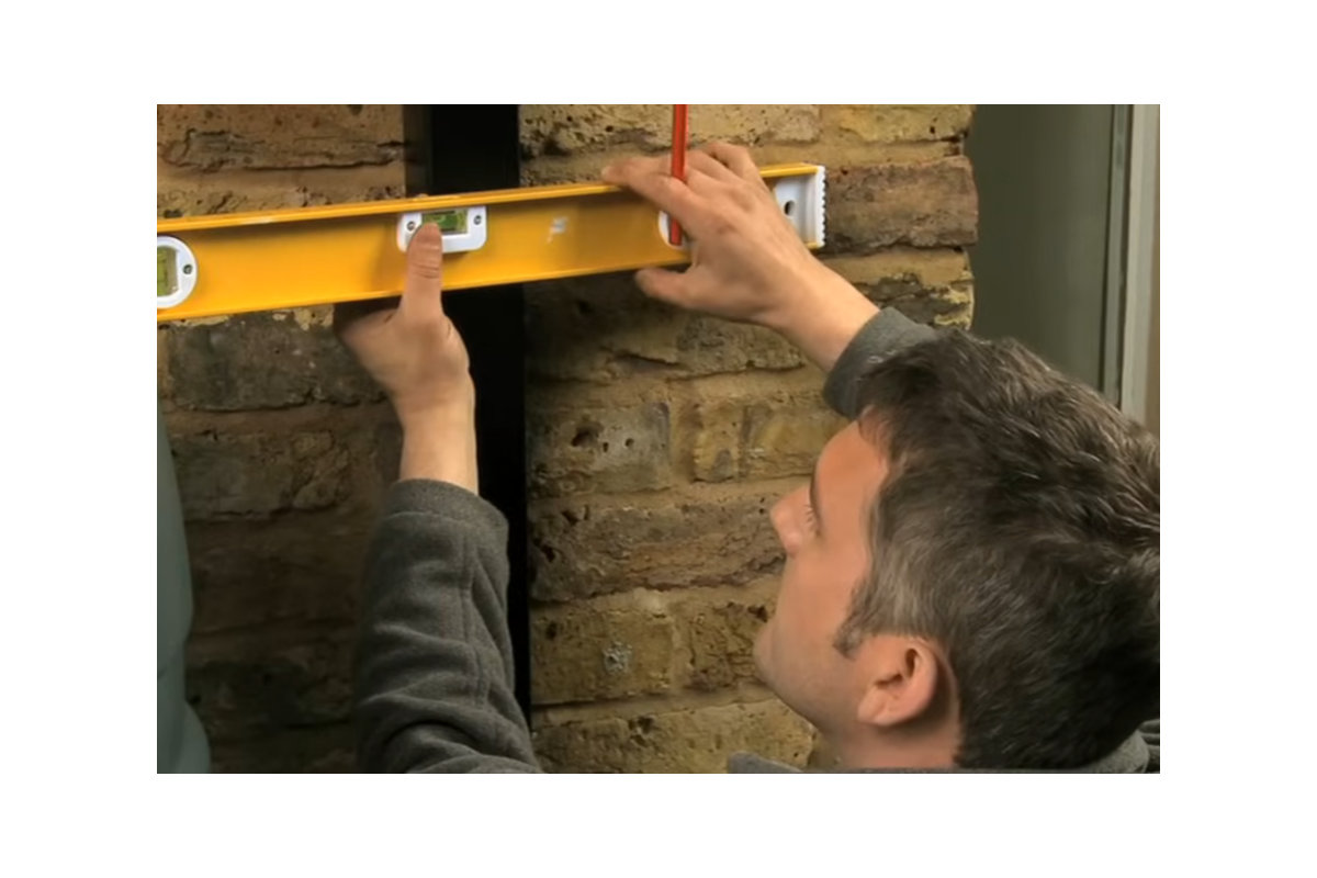 A spirit level being used to align a rainwater diverter beside a water butt.