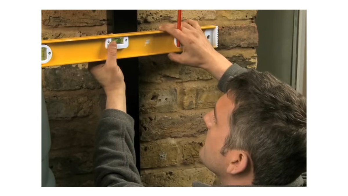 A spirit level being used to align a rainwater diverter beside a water butt.